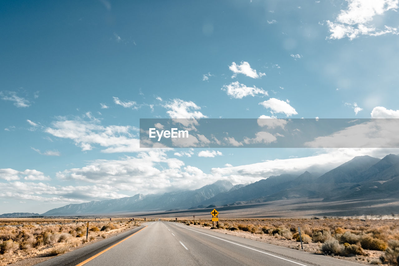 Empty road amidst field by mountain against sky