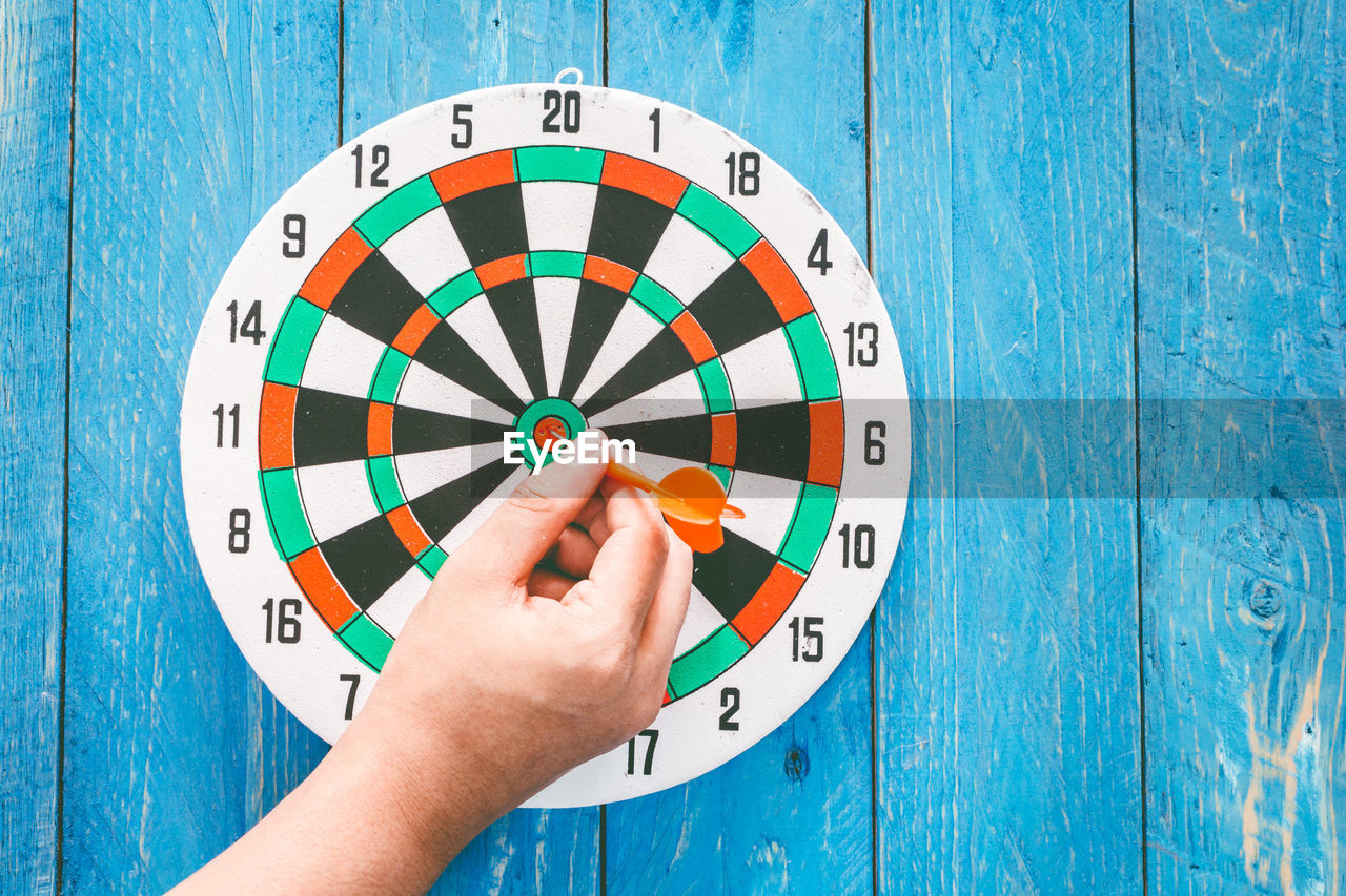 Close-up of hand removing dart from target against wooden wall