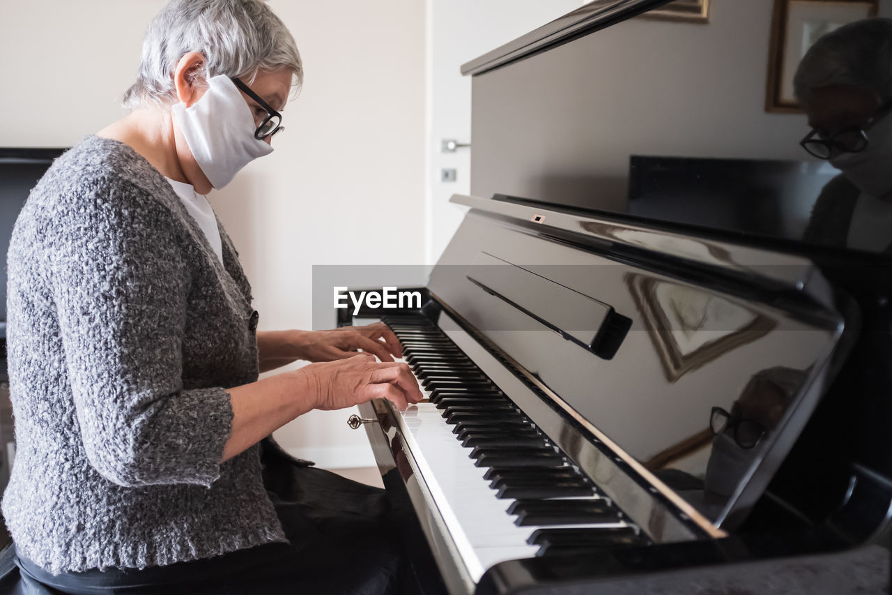  portrait of a senior woman with  face mask playing the piano at home. concept of resilience.