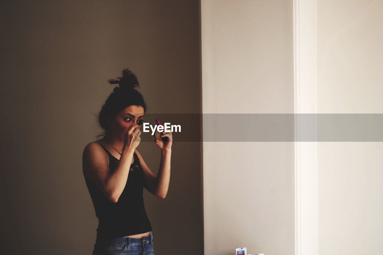 Woman applying mascara while standing at home