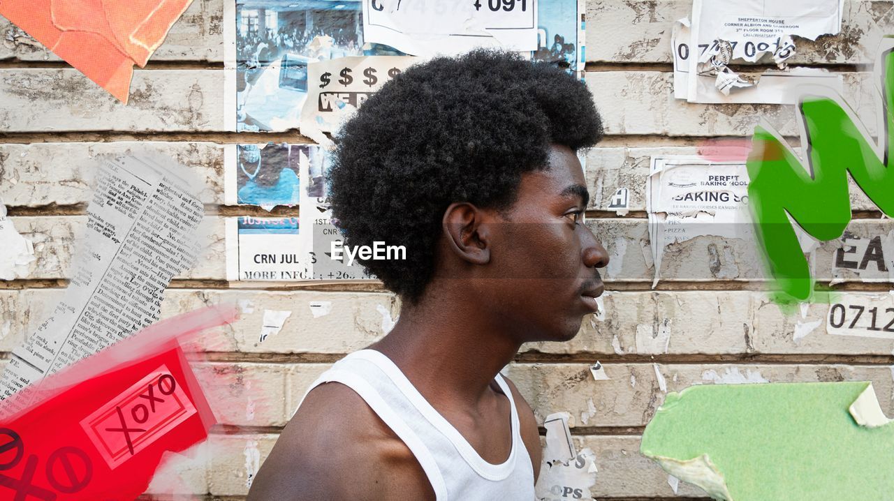 Side view of young man looking away against wall