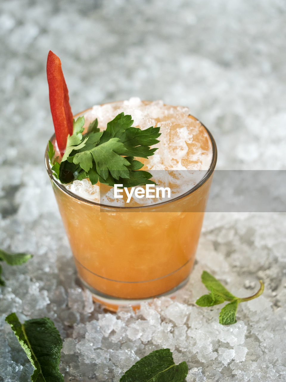 Close-up of drink garnish with bell pepper and herb in glass on crushed ice