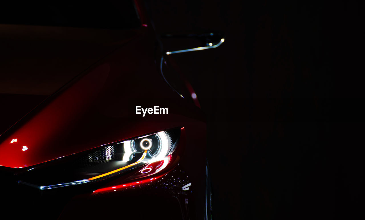 Illuminated headlight of car against black background