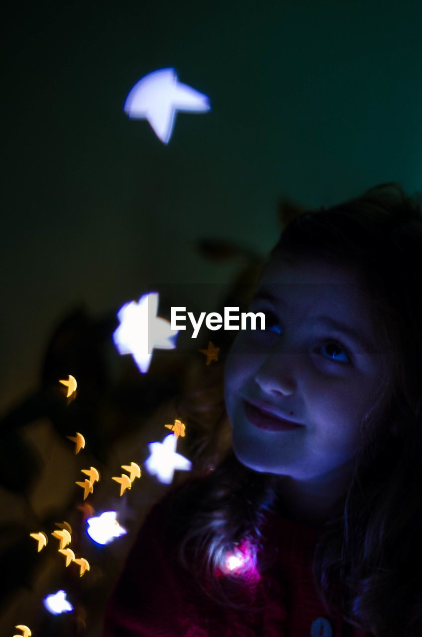 Close-up of girl with illuminated string lights at home