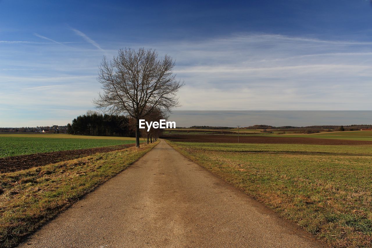 Road amidst field against sky during sunset