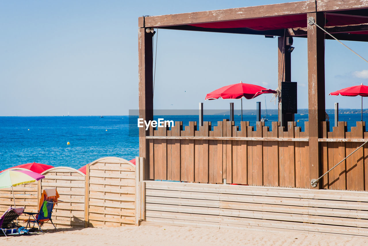 water, sea, beach, umbrella, sky, vacation, land, nature, parasol, trip, holiday, horizon, horizon over water, travel destinations, summer, architecture, relaxation, sunshade, protection, clear sky, chair, travel, sand, sunny, blue, day, sunlight, beauty in nature, security, adult, outdoors, scenics - nature, seat, shade, tourism, beach umbrella, tranquility, leisure activity, hut, men, tranquil scene, wood, walkway, ocean, women