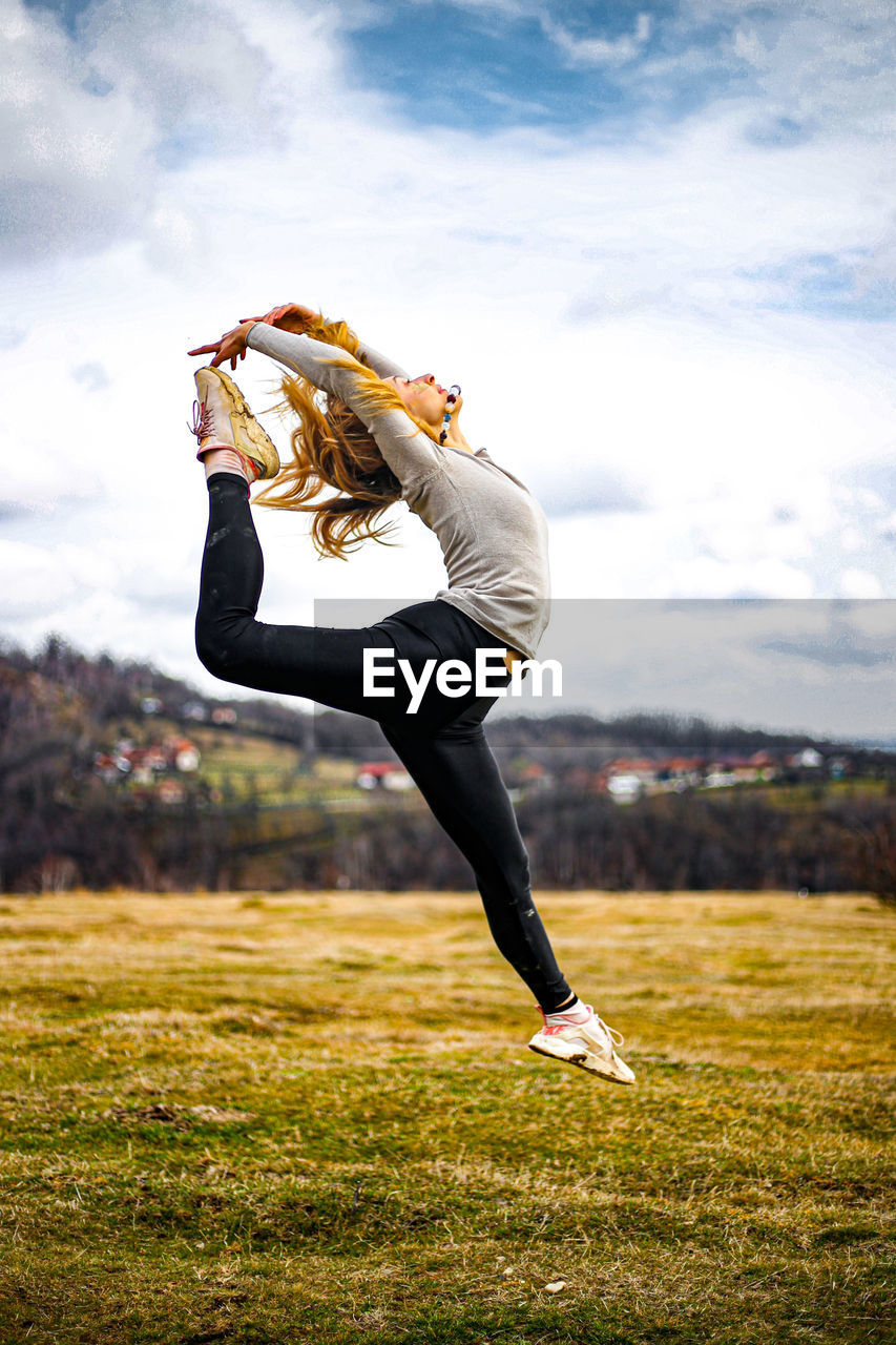 FULL LENGTH OF YOUNG WOMAN JUMPING ON FIELD