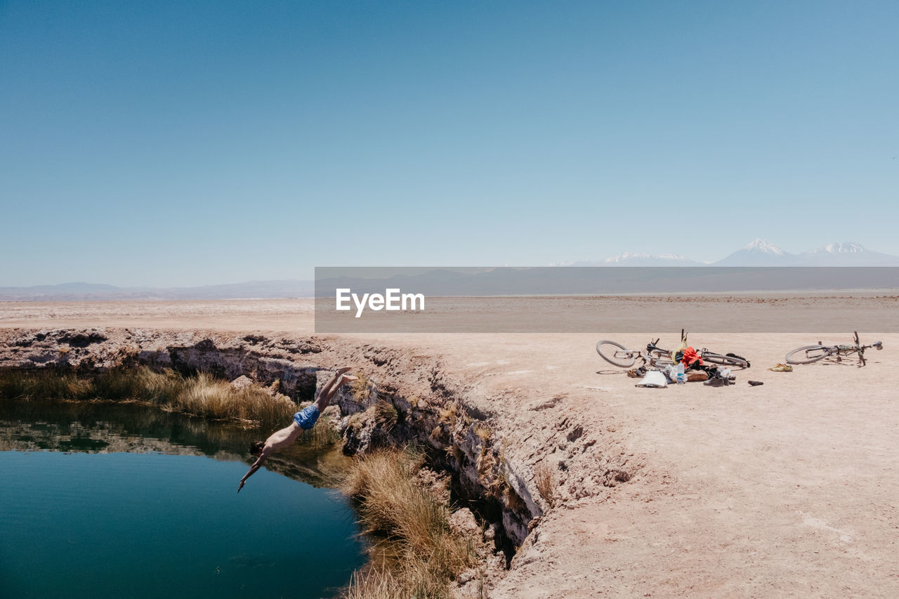 Shirtless man jumping in lake at desert