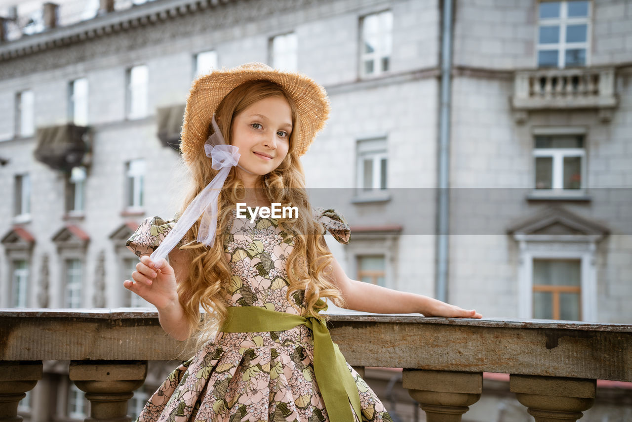 Little girl in dress and hat posing on the balcony