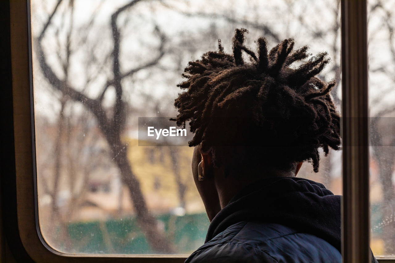 Rear view of man looking through window while sitting in bus