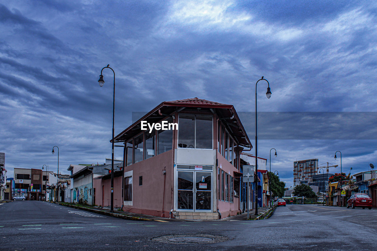 EMPTY ROAD AMIDST BUILDINGS AGAINST SKY