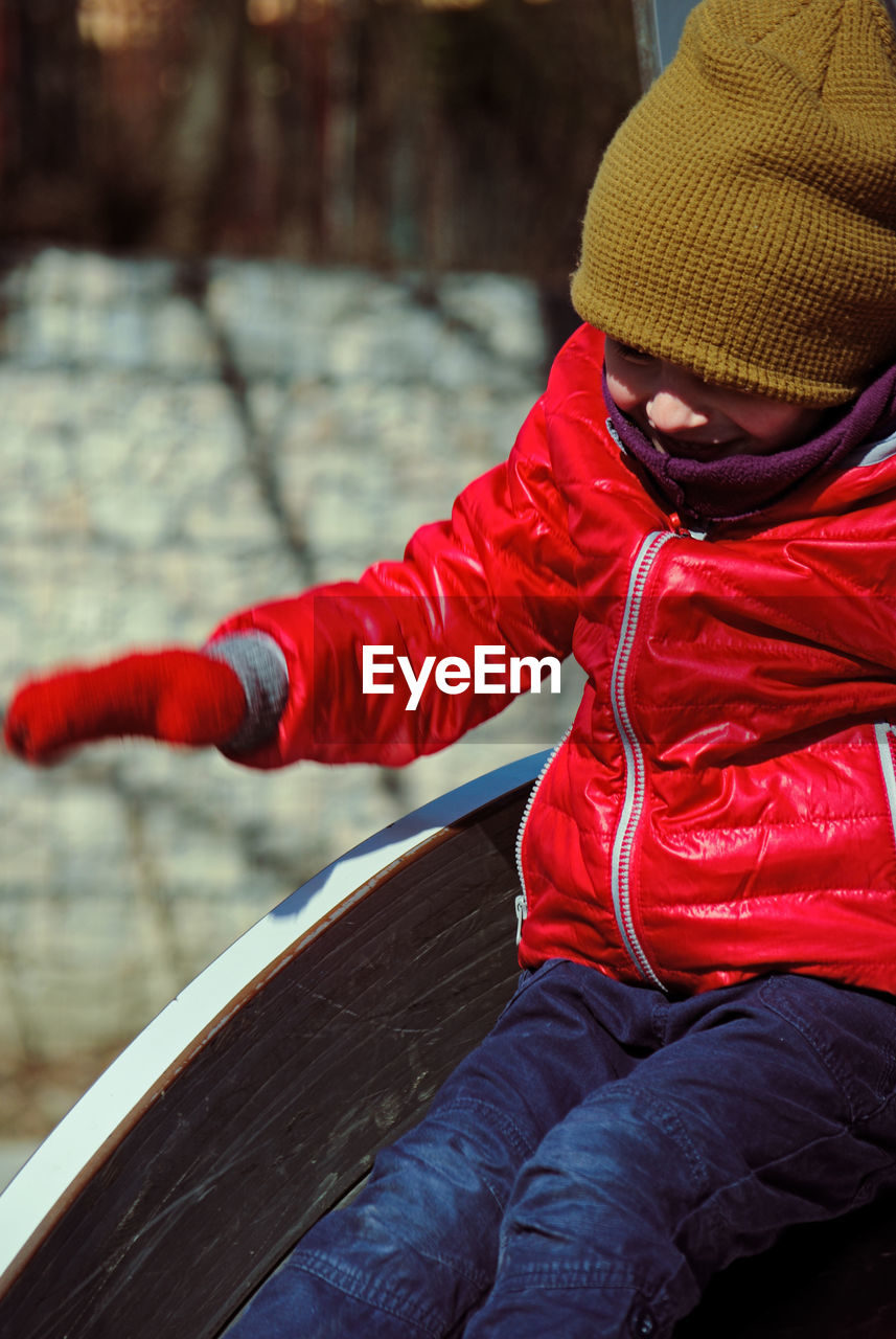 Cute boy wearing warm clothing while sitting on slide in playground