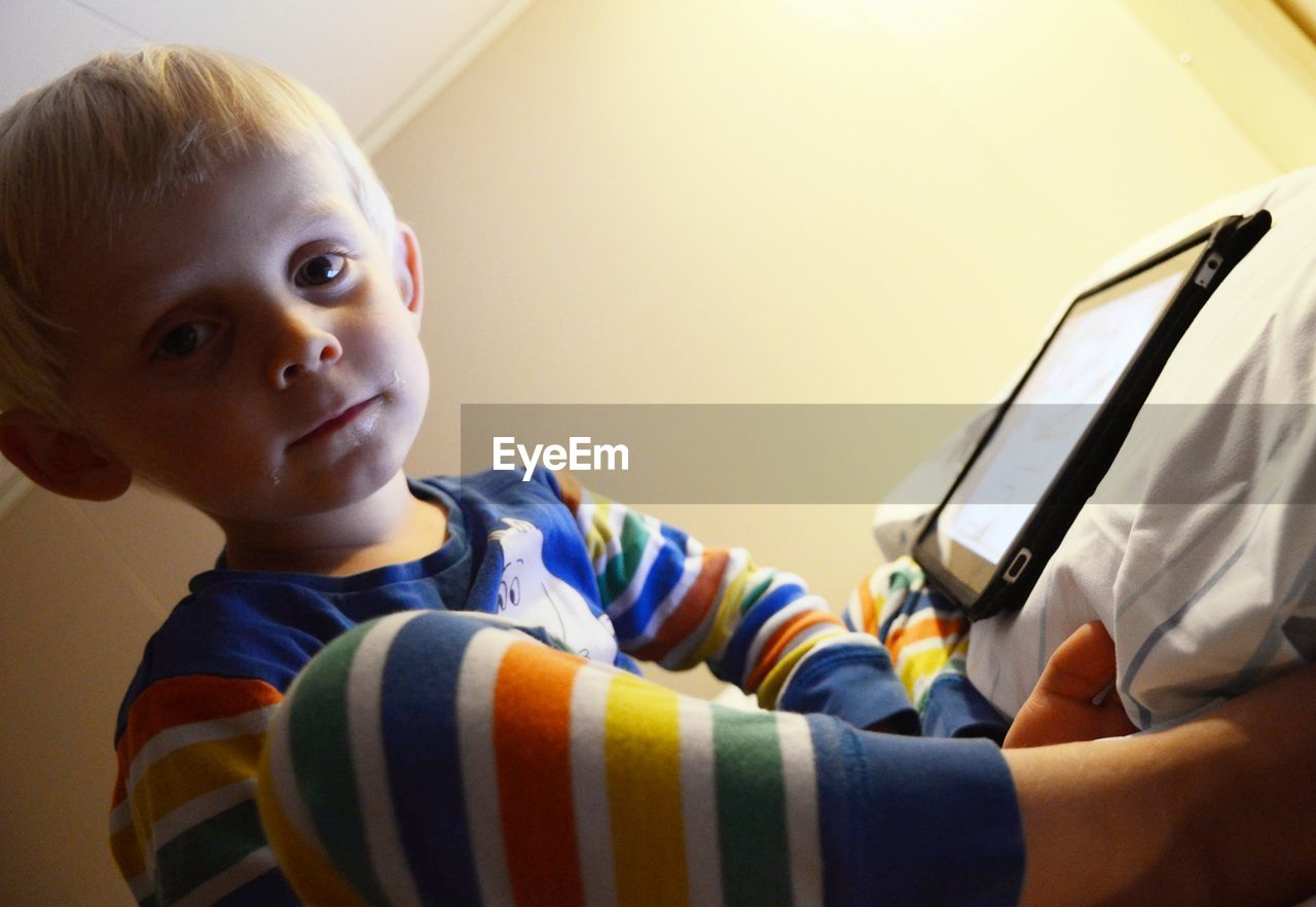 Low angle portrait of cute boy with digital tablet sitting at home