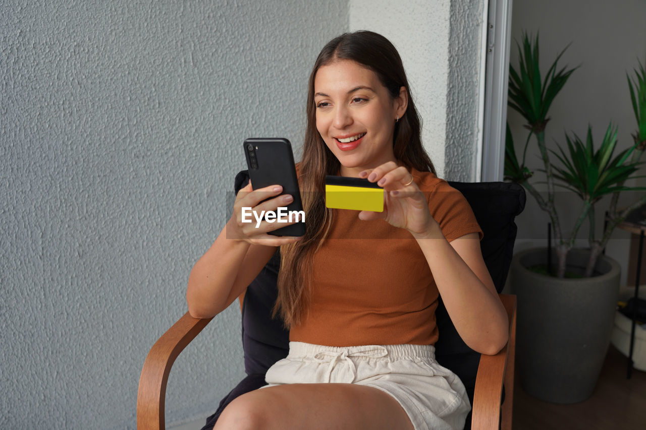 Smiling pretty woman watching phone showing credit card to camera