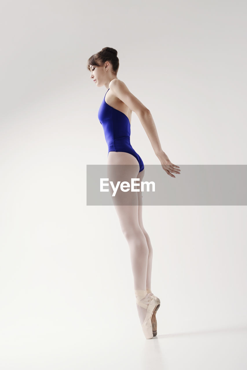 A ballerina in a bodysuit and pointes poses in a photo studio in motion showing beautiful long legs