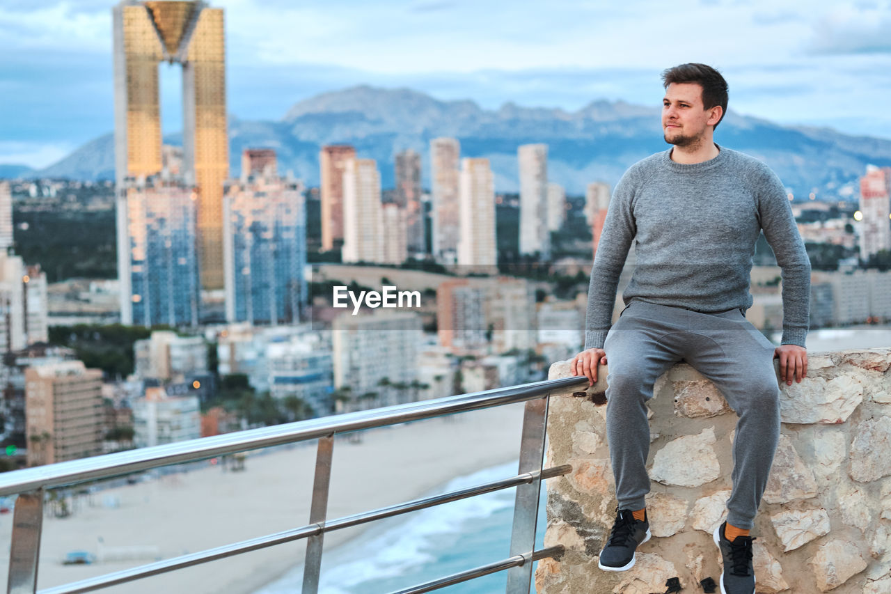 MAN ON RAILING AGAINST CITYSCAPE