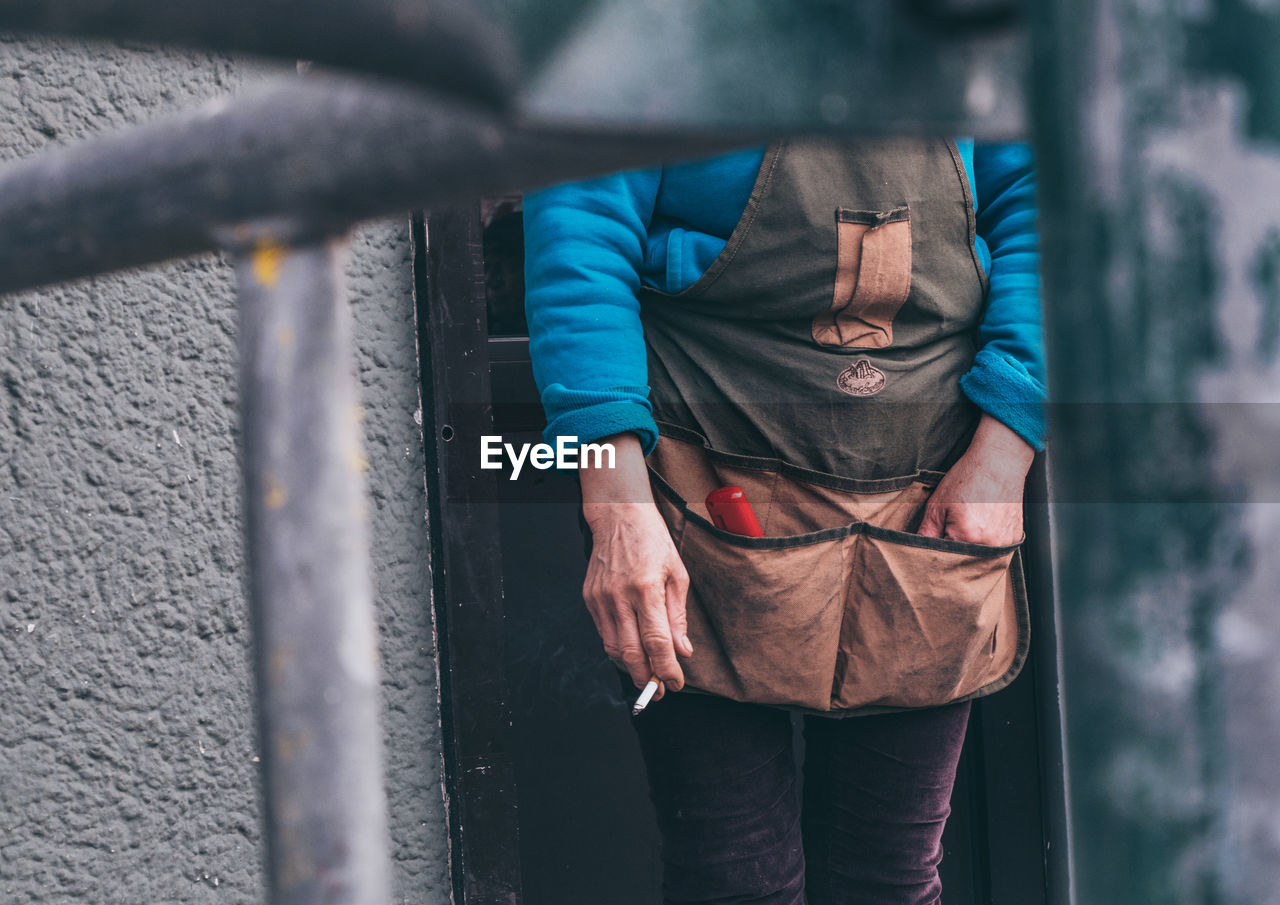 MIDSECTION OF MAN HOLDING UMBRELLA WHILE STANDING BY METAL