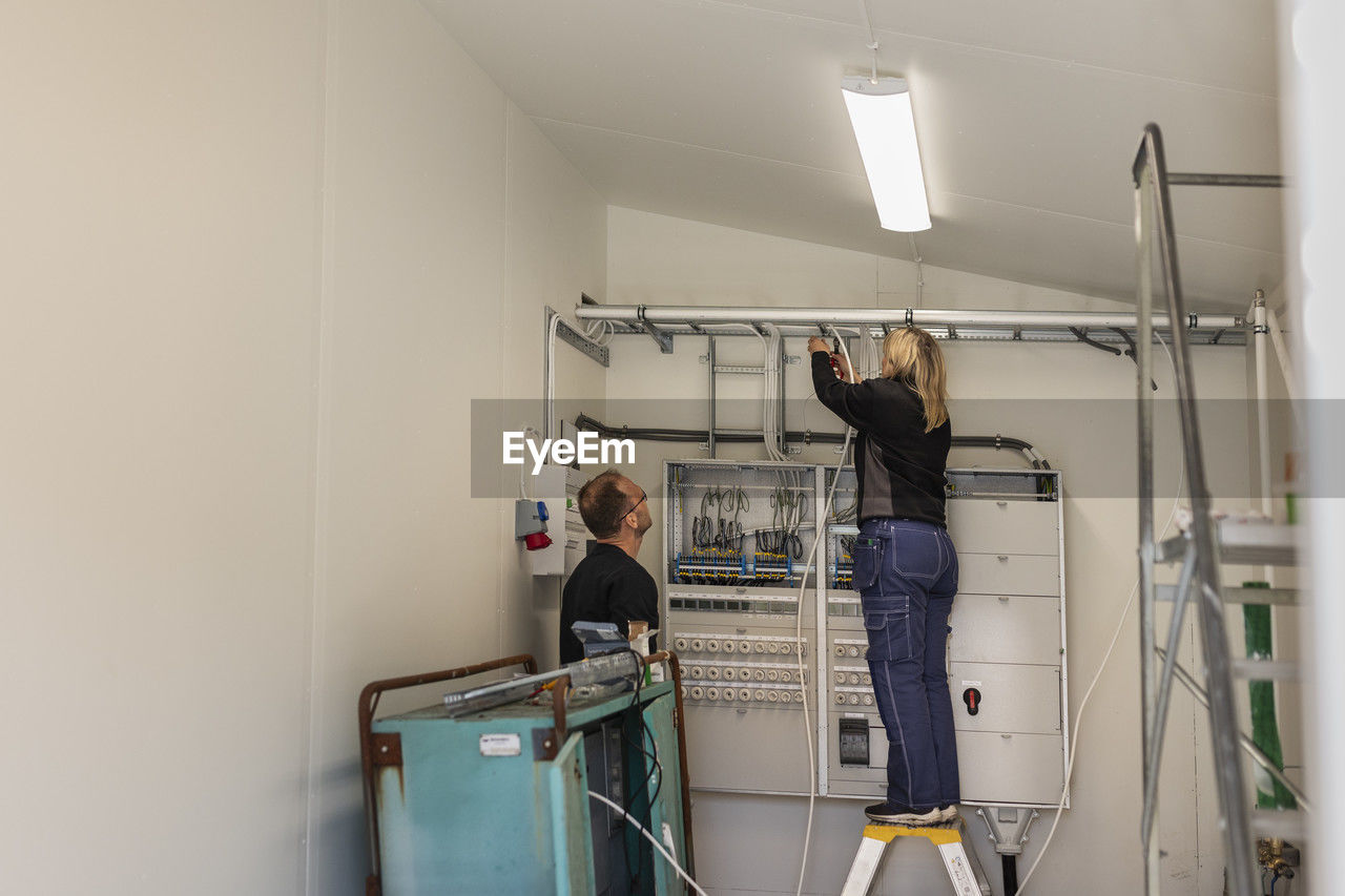 Female electrician installing cables standing by male coworker in meter room