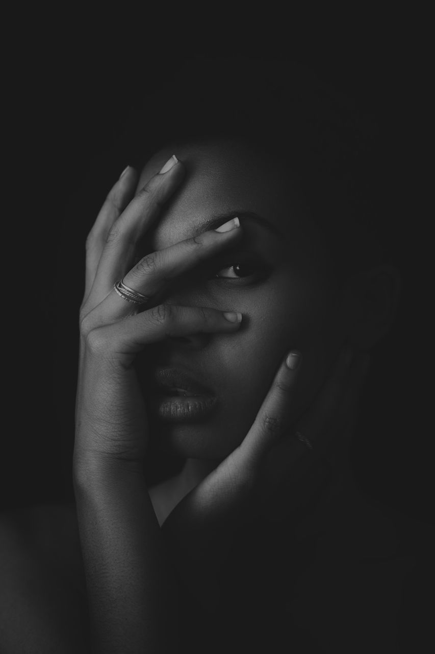 Portrait of woman covering face with hands against black background