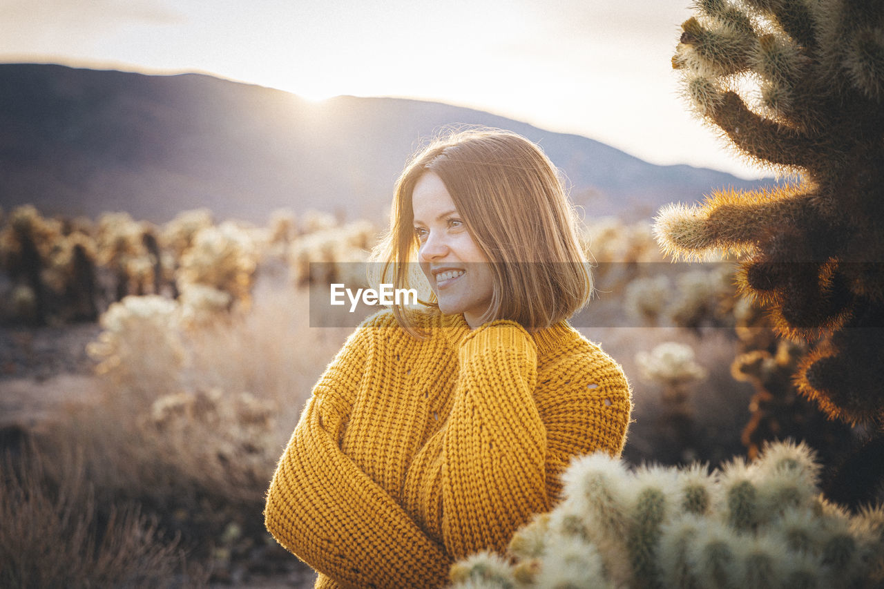 A woman is standing near a cactus in the desert of california