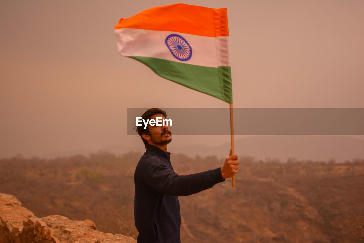 Man holding indian flag on mountain against sky