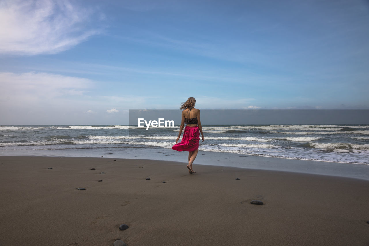 Rear view of woman on beach against sky