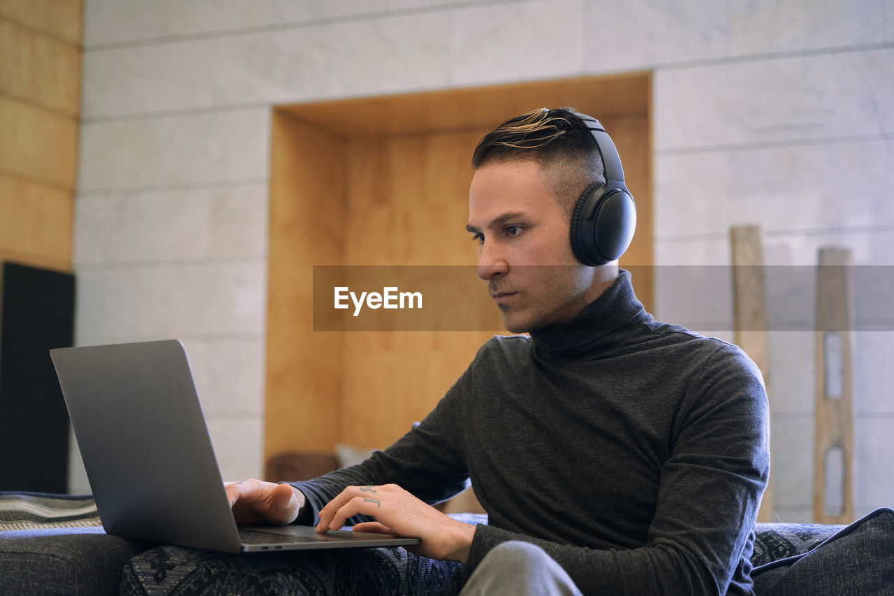 Young businessman in headphones having video call via netbook at hotel lobby