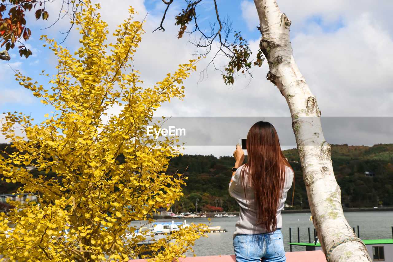 REAR VIEW OF YOUNG WOMAN STANDING AGAINST TREE
