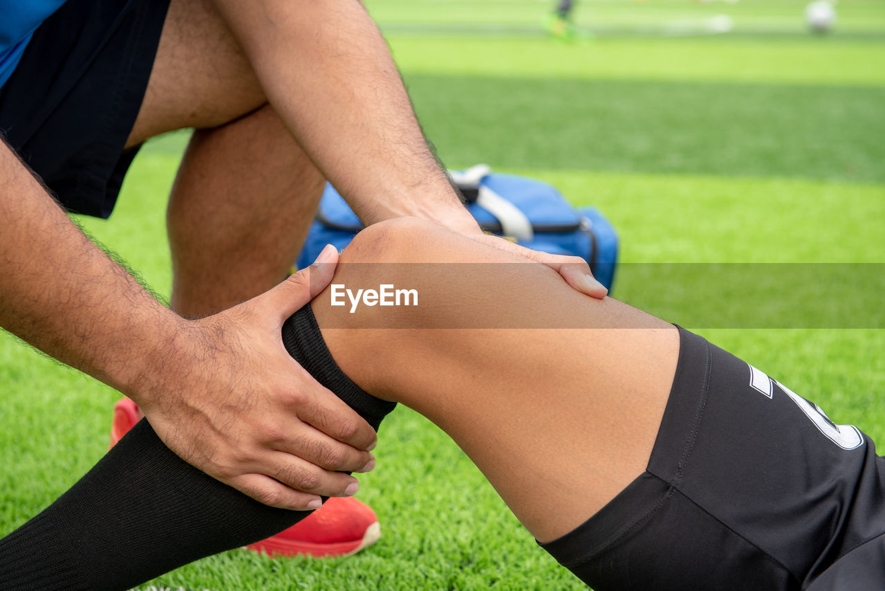 Low section of male physical therapist rubbing soccer player knee on field