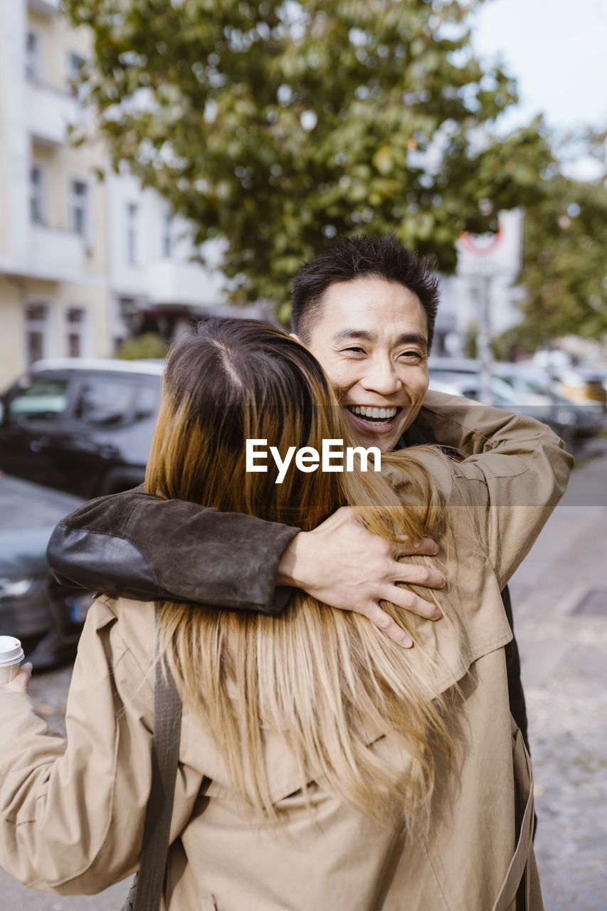 Happy male friend embracing female friend with highlighted hair