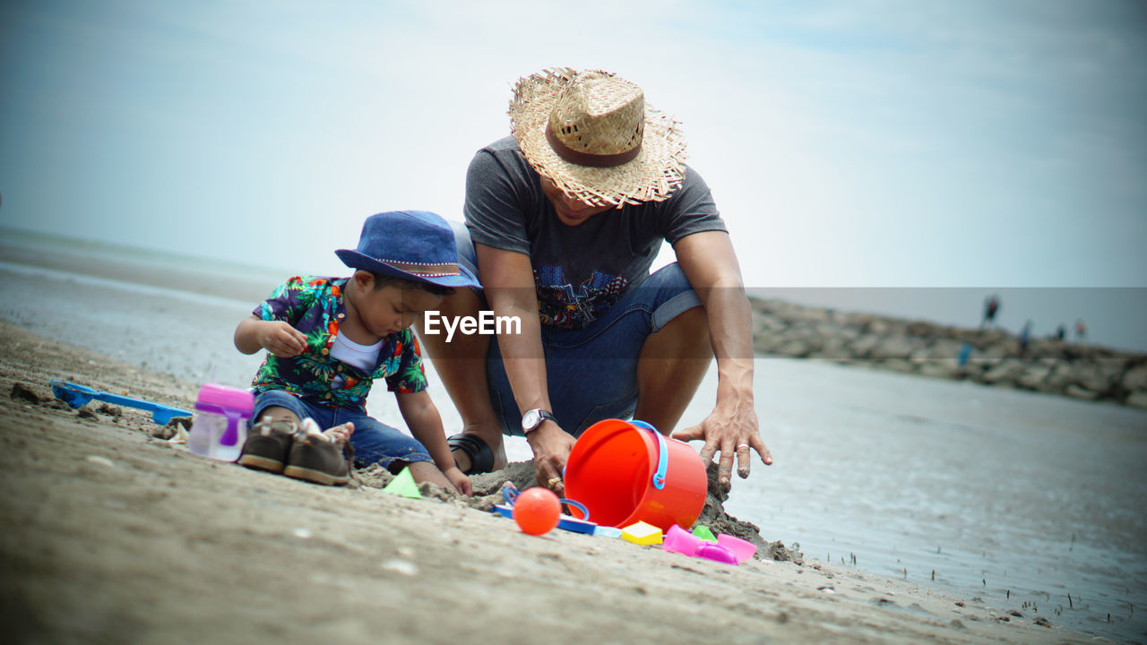 Father and son playing with toys at beach against sky