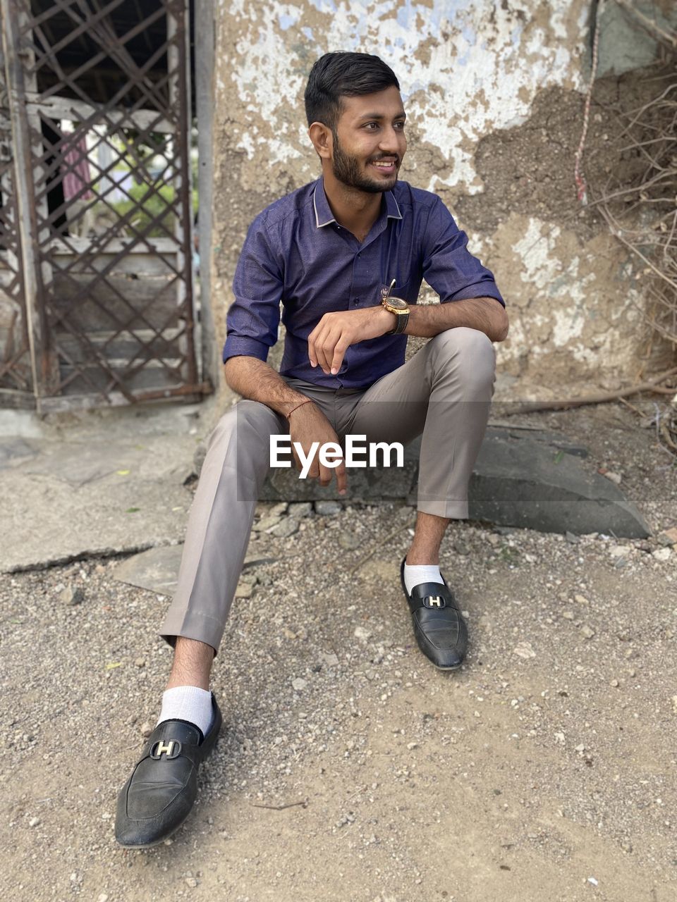 FULL LENGTH PORTRAIT OF YOUNG MAN SITTING ON WALL