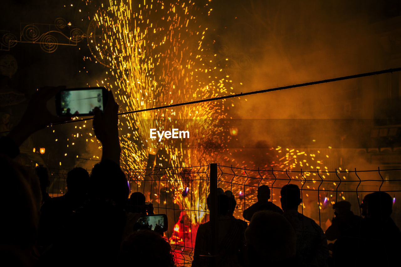 Silhouette people photographing firework display at night