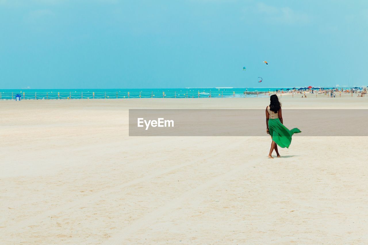 Rear view of woman walking at beach against clear sky