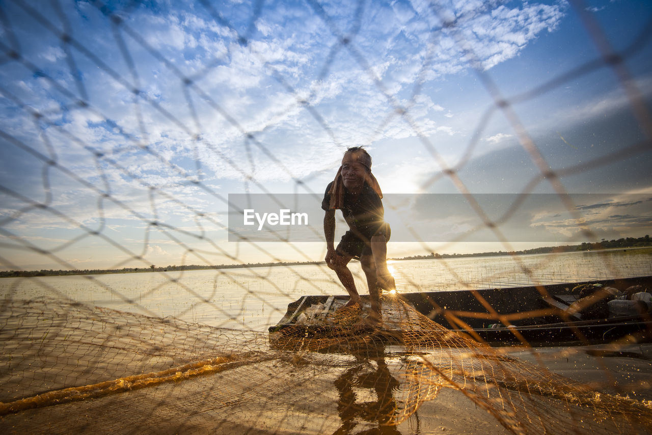 Fisherman holding fishing net at sea against sky