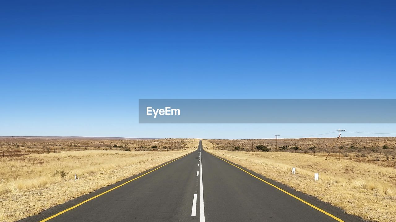 Road leading towards landscape against clear blue sky