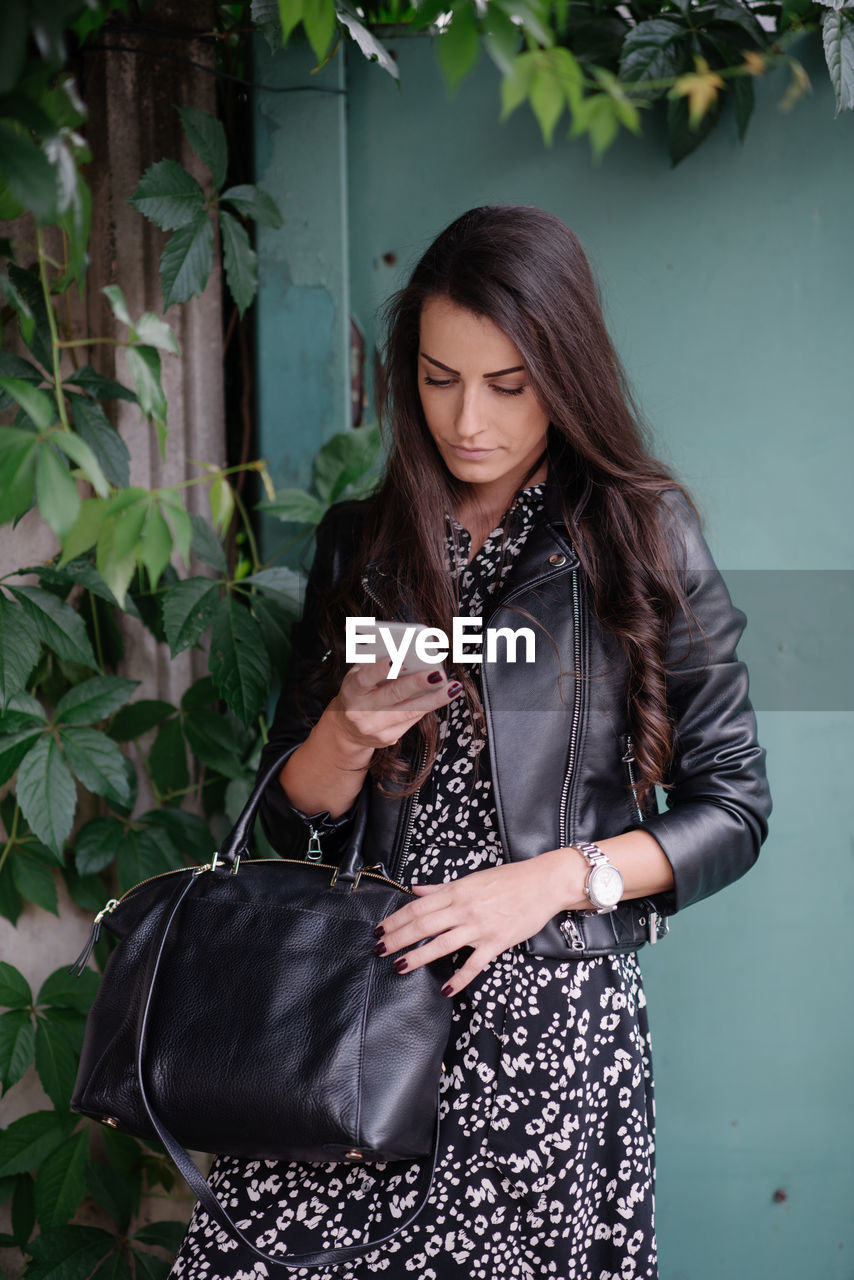 Beautiful young woman with leather jacket looking at her smart phone.