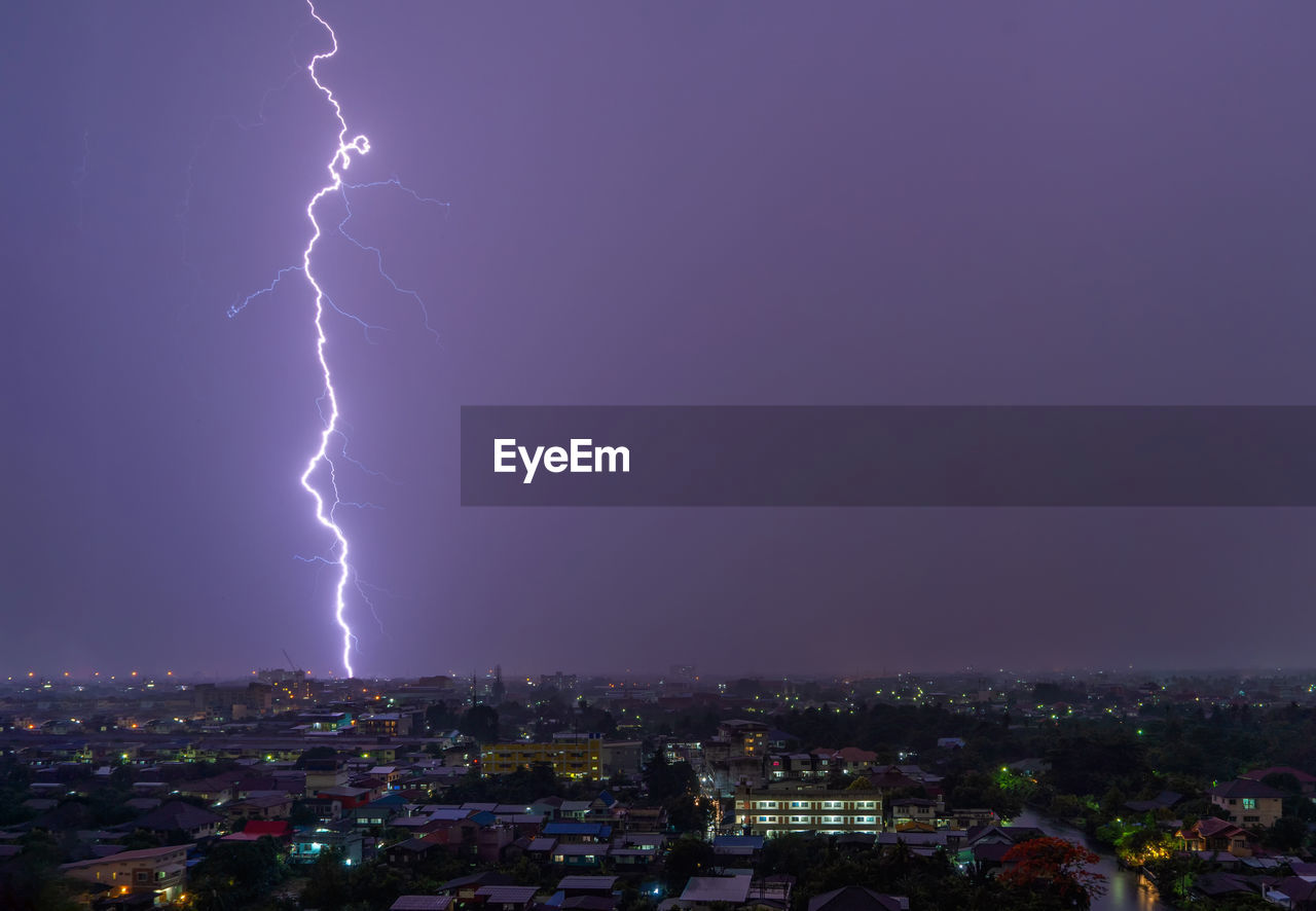 Lightning over illuminated city against sky at night