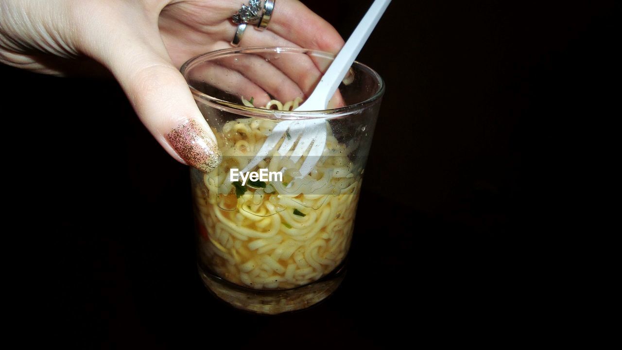 Cropped hand holding cup noodles against black background