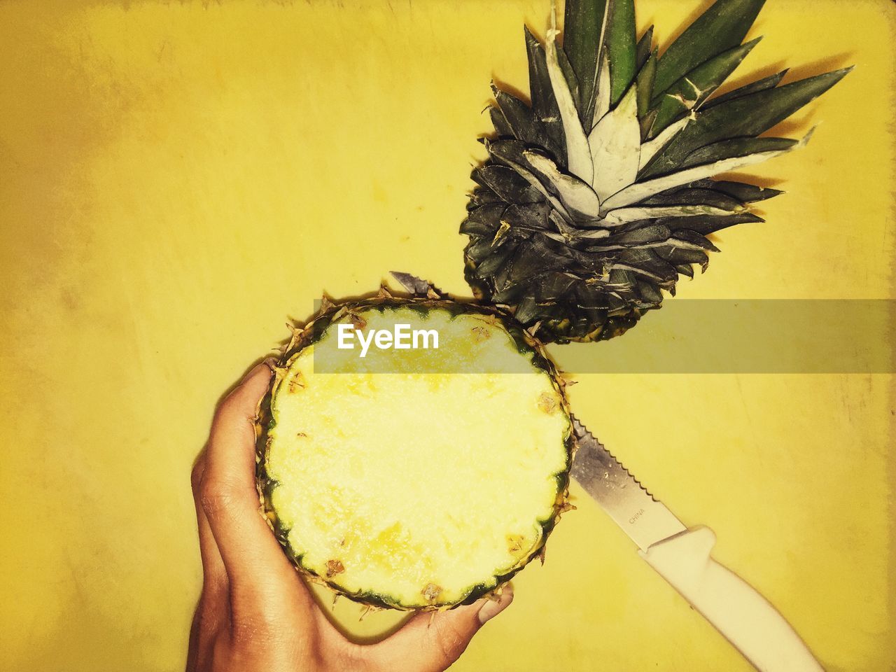 Cropped image of person holding chopped pineapple against yellow table