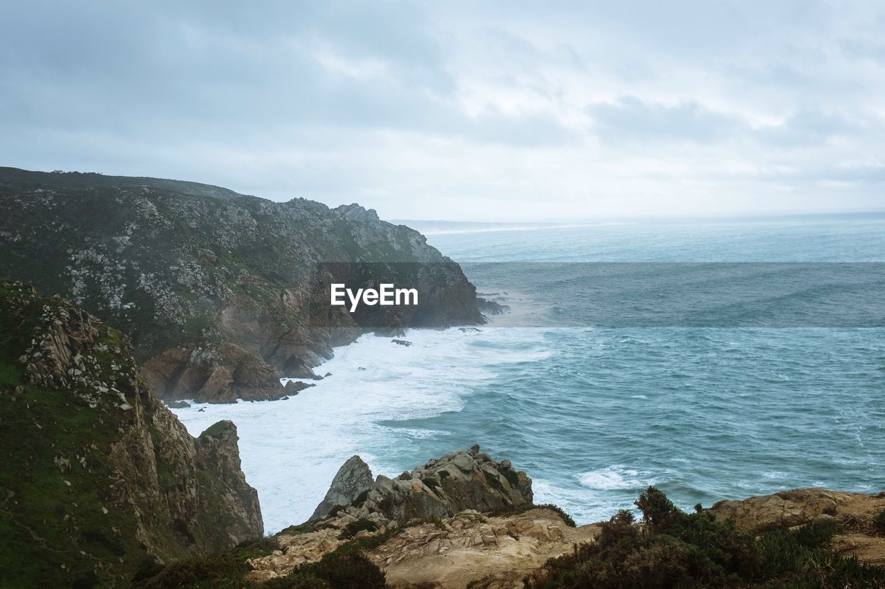 Scenic view of sea by cliff against sky