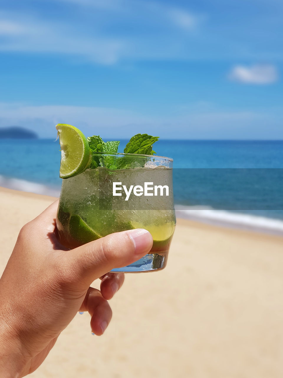 CROPPED IMAGE OF HAND HOLDING DRINK AT BEACH