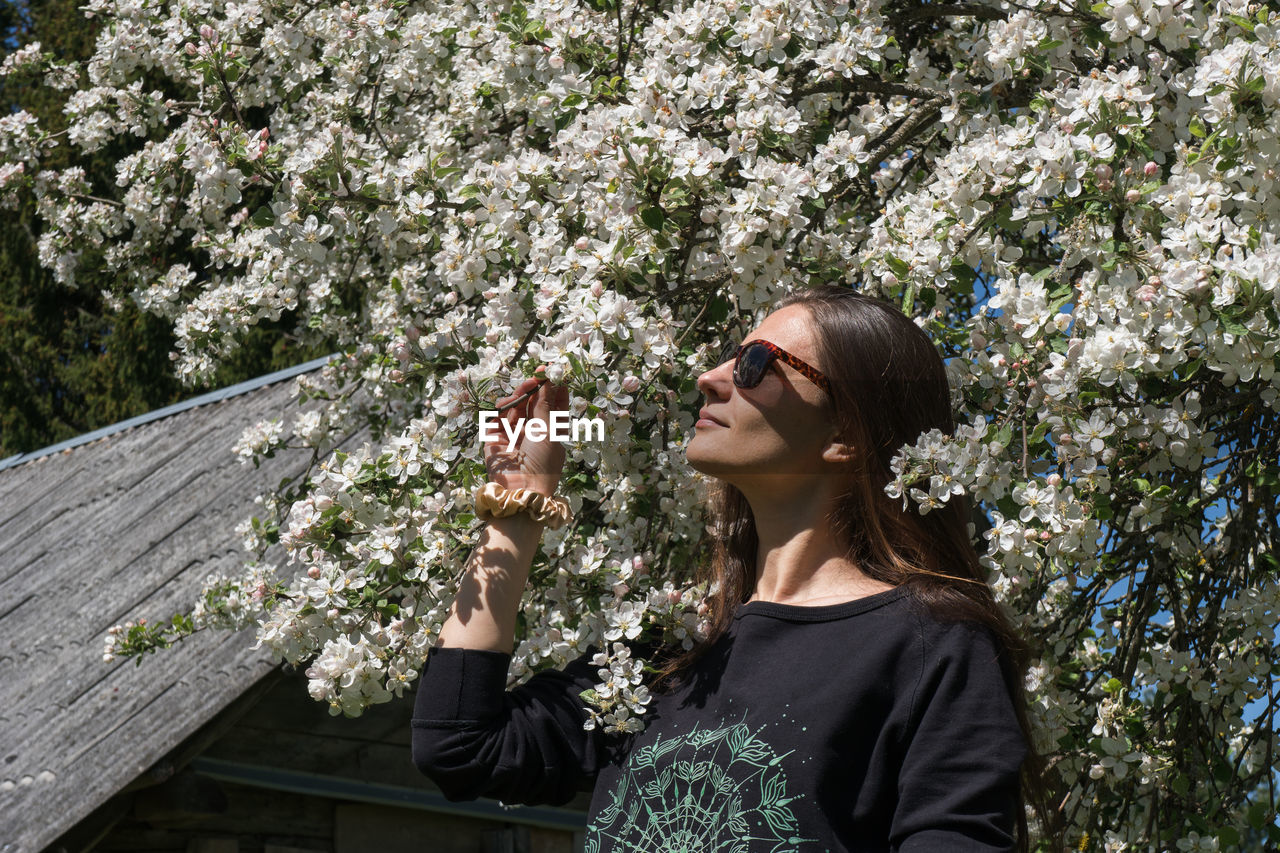 WOMAN STANDING BY FLOWERING PLANTS