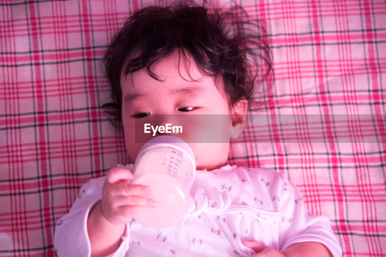 Close-up of cute baby holding milk bottle while lying on blanket