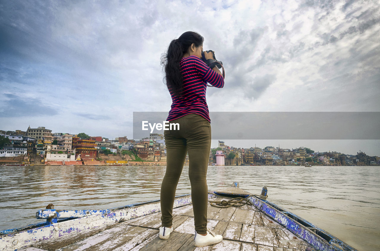 Rear view of woman photographing while standing on boat in river