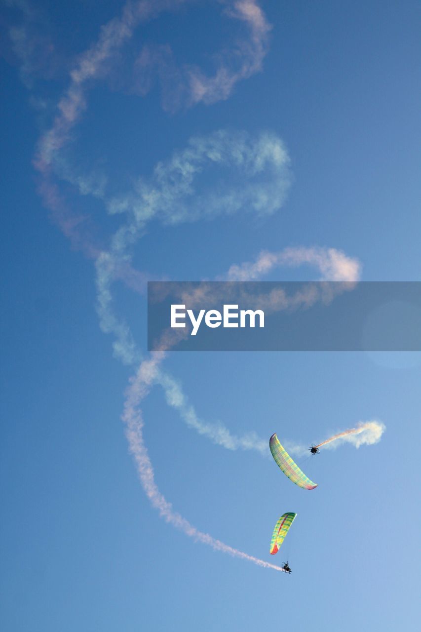 Low angle view of people paragliding against blue sky