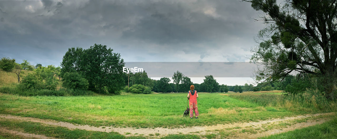 A woman with a dog stands in front of a quiet, lonely landscape near berlin in germany