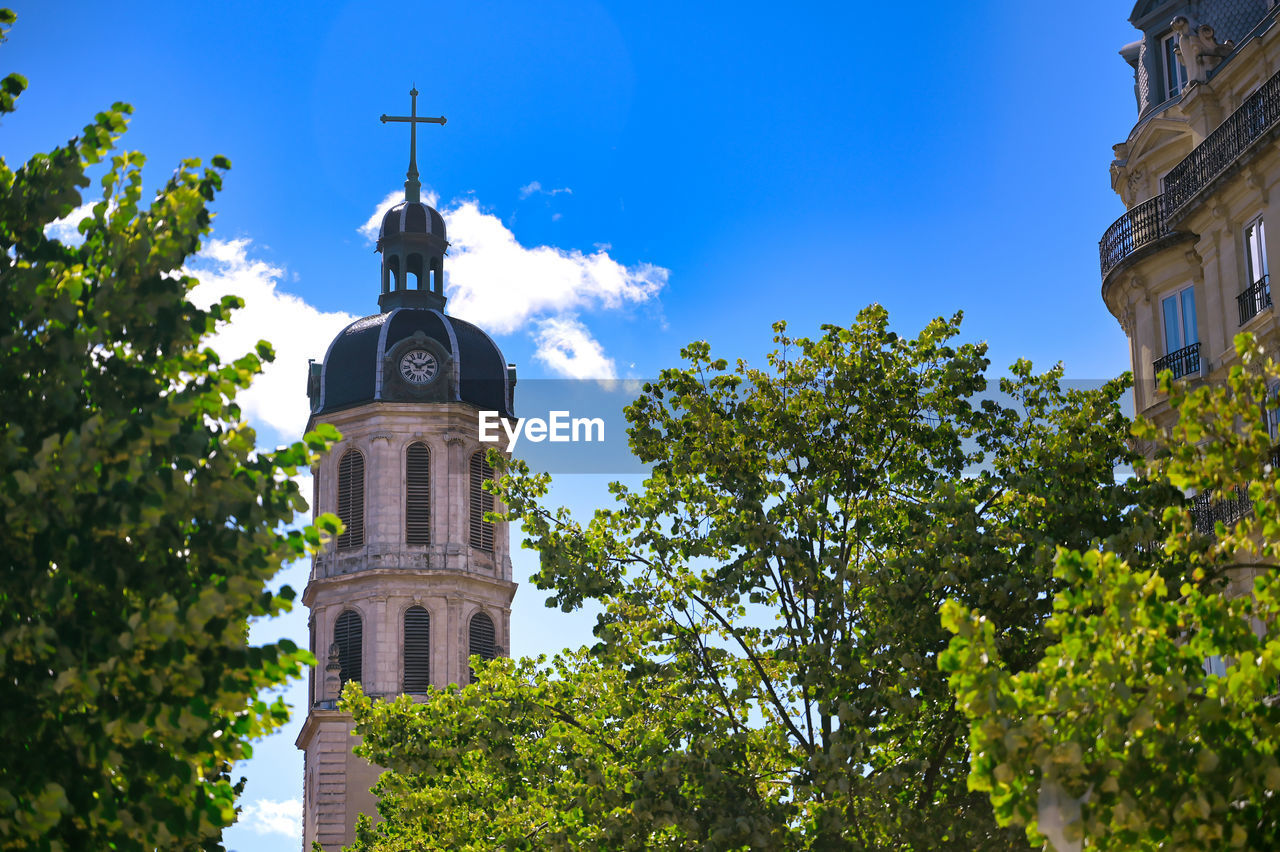 LOW ANGLE VIEW OF CLOCK TOWER AMIDST TREES AND BUILDINGS AGAINST SKY