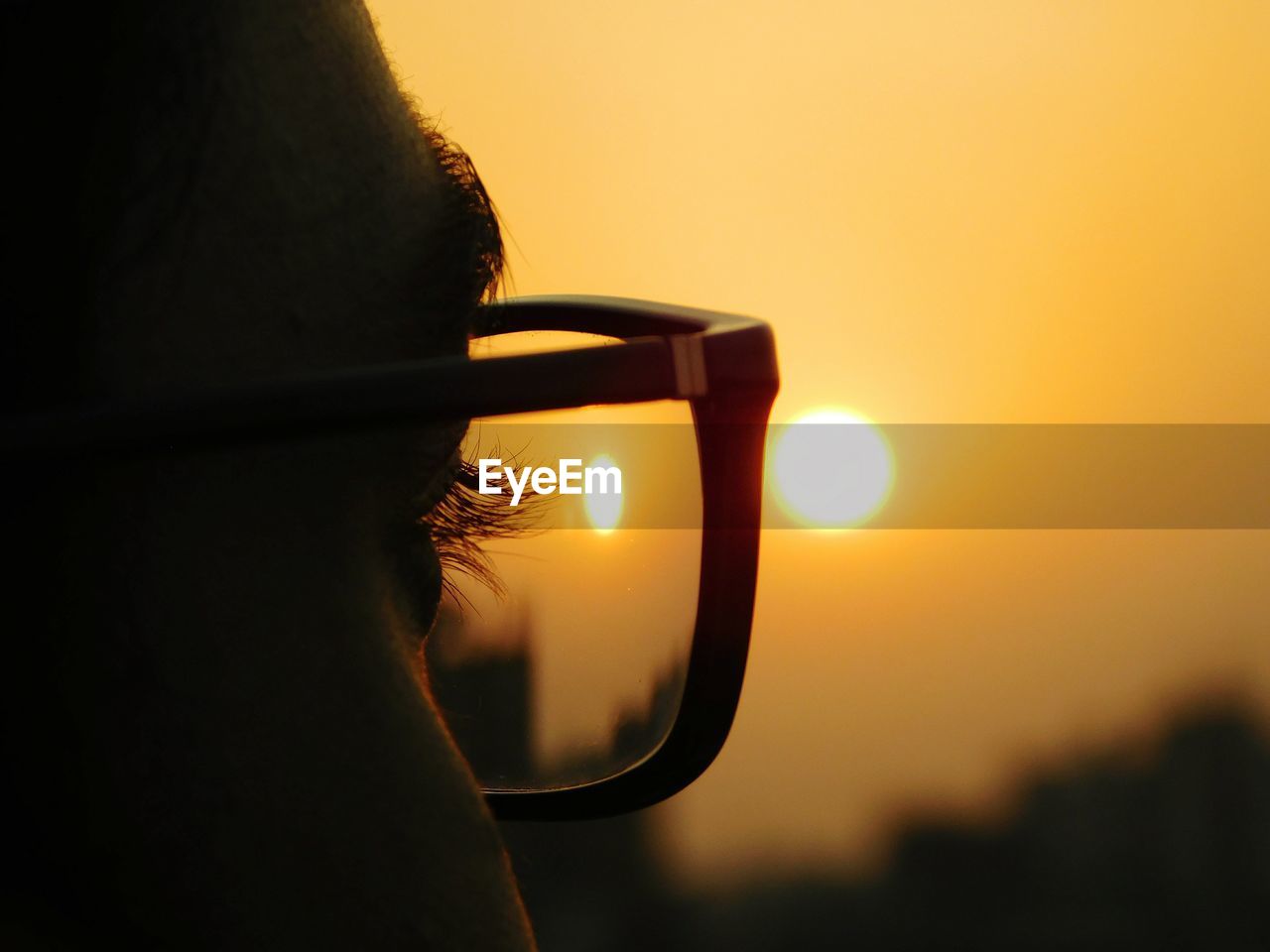 Close-up man eye against orange sky during sunset