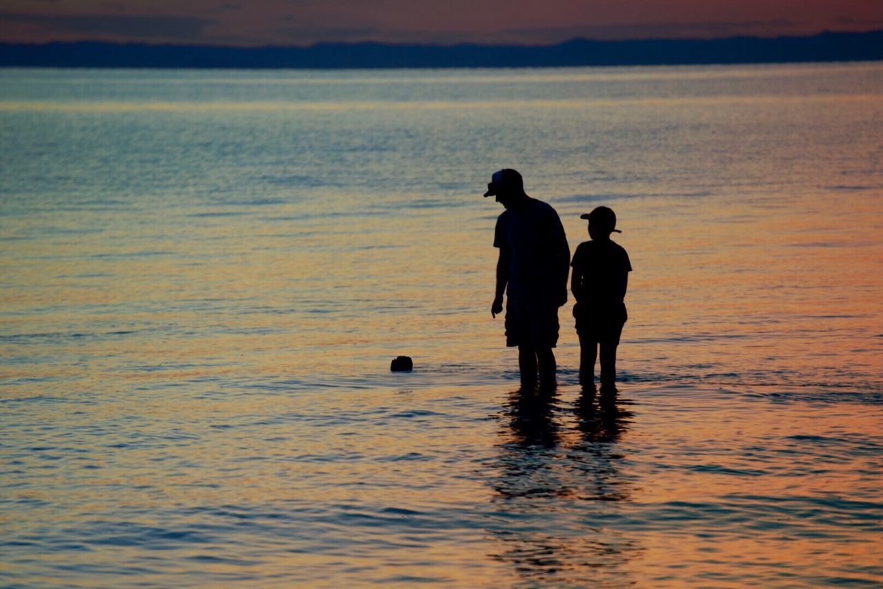 Rear view of friends standing in sea at sunset